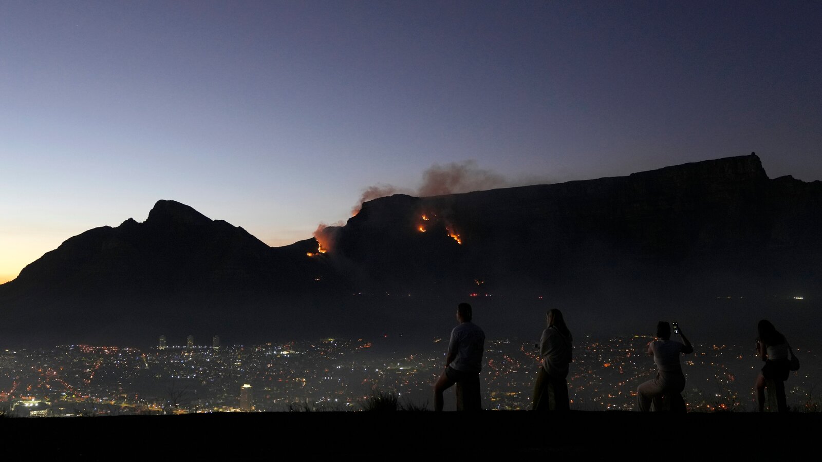 People watching a mountain fire above a city at night